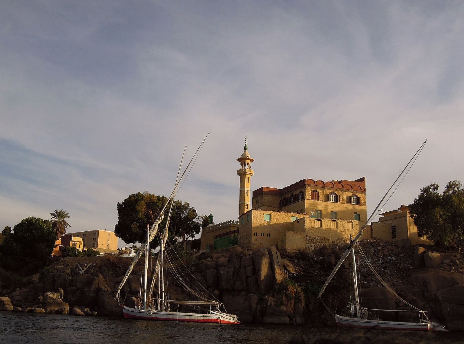 Feluccas moored below a riverside mosque at sunset in Aswan