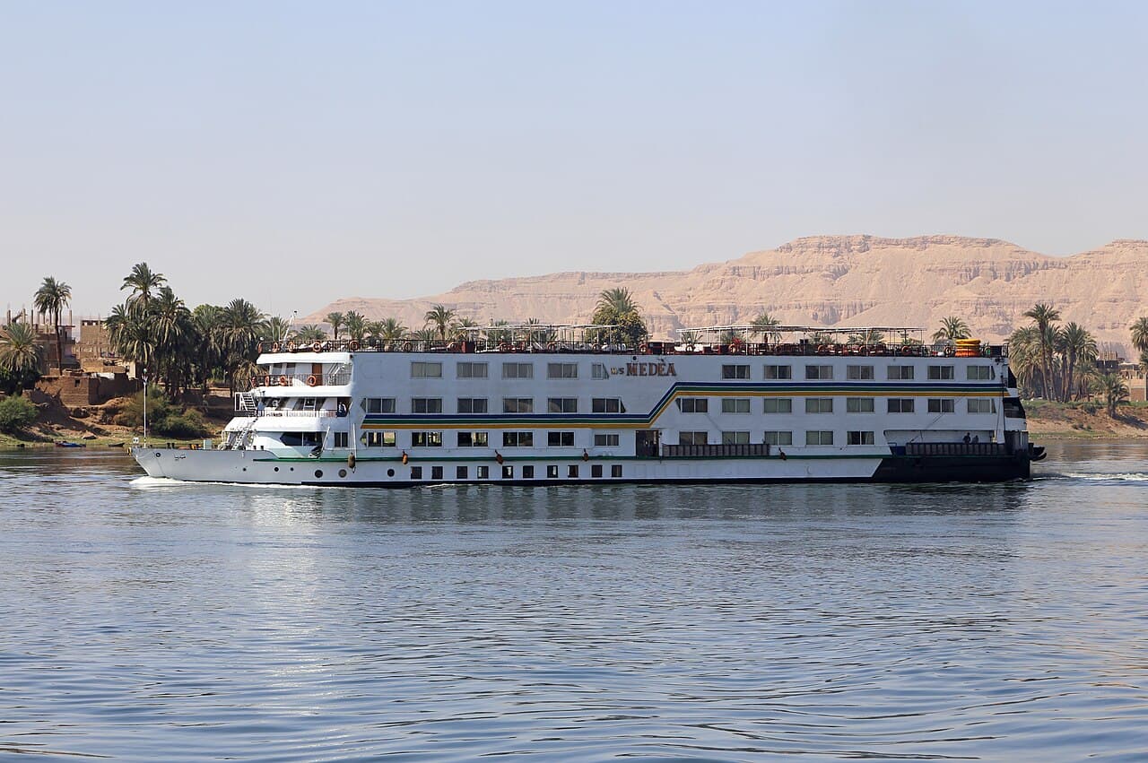 A Nile cruise ship sailing past palm trees and desert hills